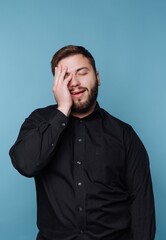 Obraz premium Man expresses a light-hearted moment while standing against a blue background in a simple black shirt and relaxed posture