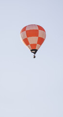 Bright orange and white checkered hot air balloon with a passenger basket soaring in a clear, serene sky.