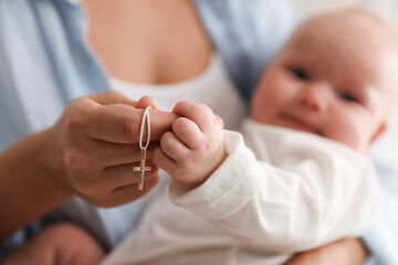 Sacrament of baptism. Woman holding little baby and gold cross indoors, selective focus