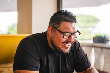 Plus size Latino man with glasses and beard laughing spontaneously in a restaurant