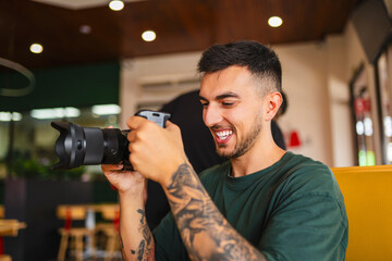 Young tattooed photographer reviewing photos on camera screen in a coffee shop