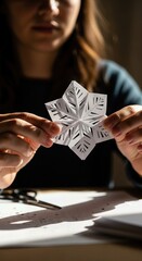 Delicate white paper snowflake held gently by hands, revealing its intricate design for joyful winter holiday decoration creation. A peaceful seasonal craft activity on a warm bright desk.