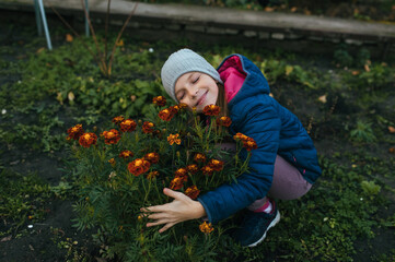 Photograph, portrait of a child, teenage girl in a garden, vegetable garden with plants, with many flowers, marigolds, autumn, outdoors.