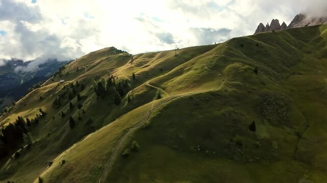 aerial golden ridges dolomites dusk glide; filmmaker captures soft evening light sweeping over rolling green hills, lone walker imagines route along ridge trail with dramatic cloudbanks