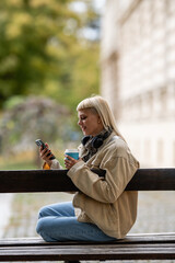 Young woman relaxing on park bench checking phone