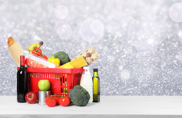 Shopping basket with products for holiday dinner on table against blurred lights. Space for text