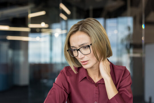 Businesswoman feeling neck pain and discomfort while working in a modern office, representing workplace stress, fatigue, and burnout from long hours and focused tasks