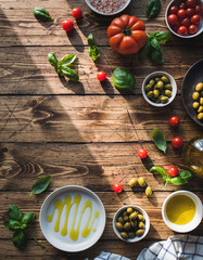 Rustic wooden table displays fresh tomatoes, basil, olives, and olive oil under dappled sunlight, ready for an Italian meal preparation