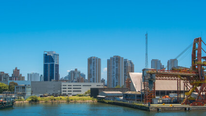Naklejka premium City skyline with modern high-rises behind an industrial port and calm blue water under a clear sky on a sunny day