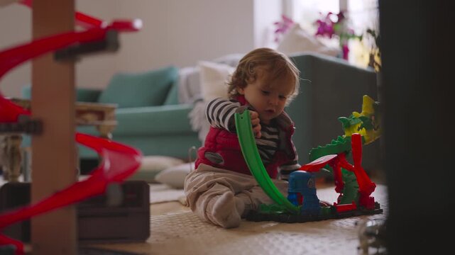 Toddler sitting on floor playing alone with colorful toy track, focused exploration imagination and developing motor skills during peaceful indoor playtime