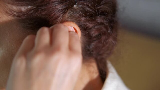 Woman inserting custom molded hearing protection earplug. Close-up view of a woman with curly hair inserting a custom-molded silicone earplug into her ear for hearing protection, reducing noise