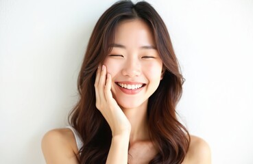 Fototapeta premium Young Asian woman touches her cheek with closed eyes. She smiles with joy and happiness. Her long brown hair frames her face. The scene highlights smooth, healthy skin.