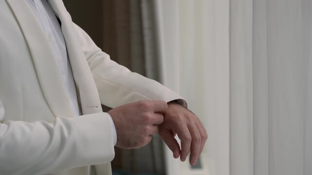 Groom Adjusting Cream Blazer By Window, Smoothing Lapel And Sleeves In Soft Daylight, Composed Reflective Moment Before Walking Down Aisle