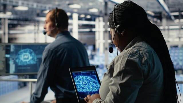 Server room tech support employee using AI on tablet to guide clients. Technician in data center helps users fix system errors on servers using artificial intelligence, camera B