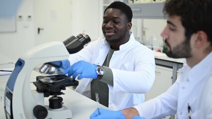 Diverse male scientists collaborating using a microscope - Powered by Adobe