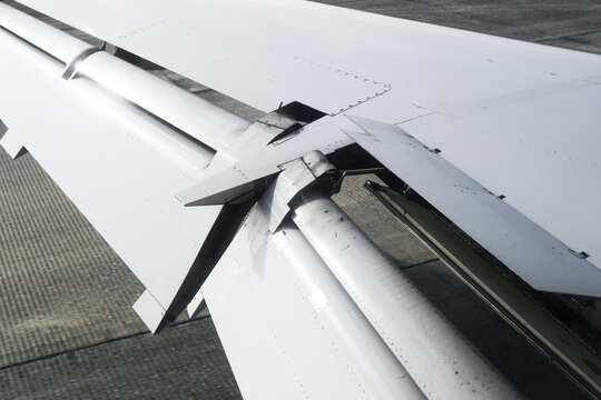 Airplane wing closeup during flight. White aircraft wing with flaps and metal details. Aviation engineering structure view. Travel transportation concept in daylight. Modern commercial airplane detail