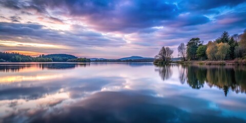 Serene lake reflecting a breathtaking sunset sky, with trees mirrored in the still water, creating a picturesque landscape of tranquility and natural beauty.