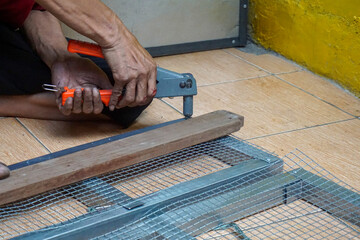 someone is working to lock the mesh iron frame using manual rivet pliers. Workers' hands and feet are clearly visible, emphasizing the technical work activity, precision, and simple fieldwork atmosphe