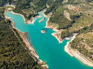 Fototapeta premium Stunning aerial photo of a turquoise reservoir surrounded by lush forest and terraced hills in South Spain, perfect for travel, nature, and landscape inspiration.