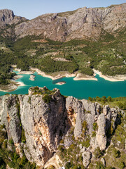 Stunning aerial photo of a turquoise lake surrounded by dramatic rocky cliffs and lush green forest in South Spain, perfect for travel, adventure, and nature backgrounds. © Flash Vector