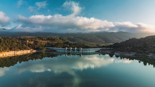 A serene reservoir and dam in South Spain, surrounded by lush hills and mountains, reflecting clouds and sky on calm water. Ideal for nature, travel, and landscape inspiration.