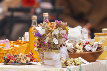 Colorful stall table at Naplavka farmers market in Prague filled with household goods, natural Christmas decorations, dried flowers, honey jars and fruit syrups, capturing festive market atmosphere.