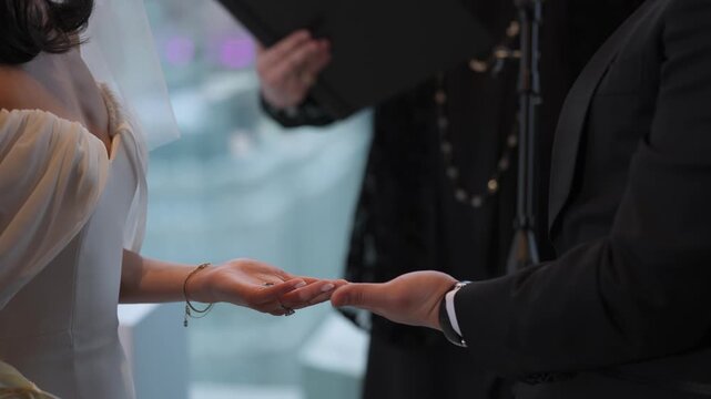 Hands Exchanging Rings At Ceremony, Officiant In Background, Bride Placing Band On Groom Finger With Focused Touch, Altar Proximity And Soft