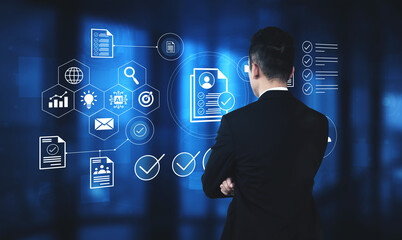 A businessman in a suit stands in a modern office, analyzing digital icons and data visualization, representing innovation and technology in business strategy. Gantry