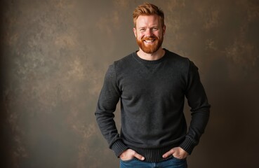 Fototapeta premium Red bearded man with short hair wears dark sweater and jeans. He smiles confidently against textured dark background. His hands are in his pockets, portraying relaxed attitude and modern masculinity.