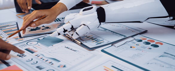 A robotic hand assists team members in a vibrant office environment, analyzing data and developing...