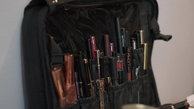 Closeup Makeup Organizer Pouch Filled With Lipsticks And Liners Pocketed Nylon Case, Metallic Tubes, Warm Studio Light, Shallow Depth