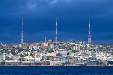 Three red and white broadcast towers on hill with uran buildings