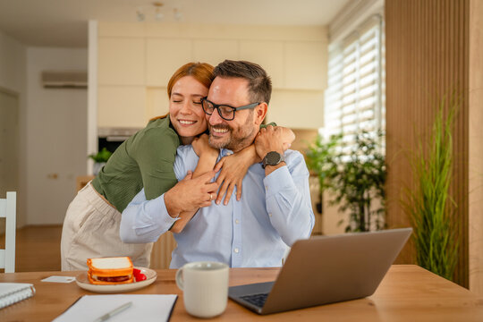 Happy couple embracing, working from home with laptop