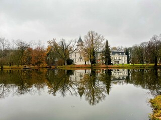 Obraz premium Beautiful autumn view of Radziejowice Palace reflected in a calm lake on a cloudy day. Location: Radziejowice, Poland.