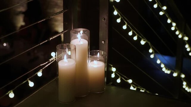 Candles On Railing With String Lights, Tall Glass Votives, Warm Flame, Deep Shadows, Dramatic Contrast, Moody Bokeh, Empty Rooftop Corridor,