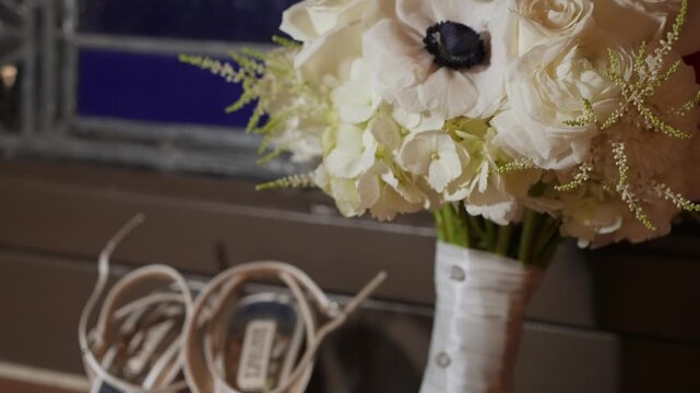 White Bridal Bouquet On StainedGlass Window, Anemone Center Framed By Roses And Hydrangea, Satin Wrapped Stems With Pearl Pins, Warm Moody