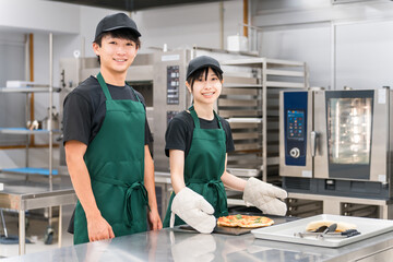 Male and female chefs taking pizza out of the oven