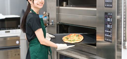 Female cook taking pizza out of the oven