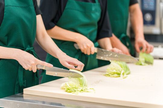 Kitchen, hands of male and female kitchen staff cutting cabbage in the back room