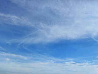 Clear blue sky with a few clouds. The sky is very bright and the clouds are scattered throughout in summer season 
