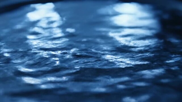 Water drips from a faucet into a sink with blurred lights reflecting in the background 