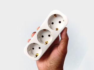A closeup image of a hand holding a multi socket power adapter against a clean white background, showing an essential electrical accessory for home, office, and daily use.