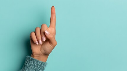 Female hand raised with index finger pointing upwards against a solid cyan background