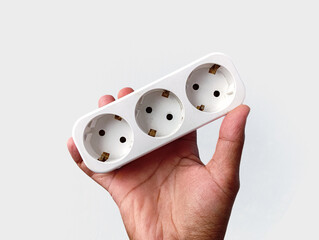 A hand holding a triple power outlet with grounded sockets, photographed on a clean white background. The image shows a practical electrical accessory for home and office power distribution.