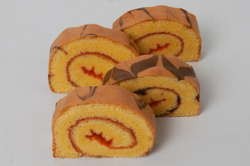 A close-up view of sliced strawberry roll cake on a white background with chocolate details and a light-colored sponge cake.