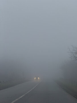 Car driving on rural road during dense fog