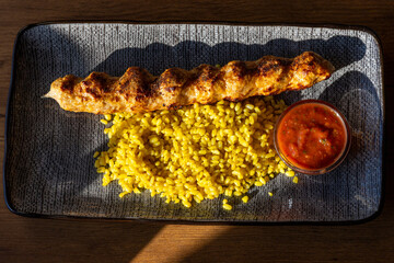Bulgur pilaf with special spices, grilled lamb kebap served with a special tomato sauce on blue plate. Top view, close up