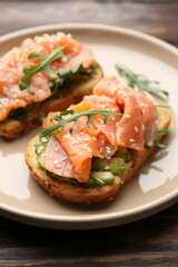Tasty bruschetta with salmon, avocado, arugula and sesame seeds on wooden table, closeup