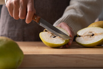 Hand holding kitchen knife and cutting pear on wooden board