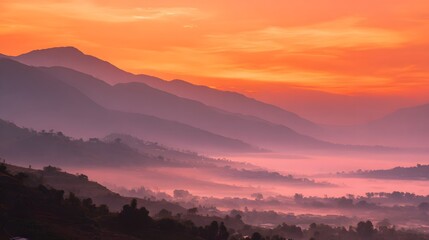 Layered mountain ranges fade into a valley filled with soft, colorful mist during sunrise
